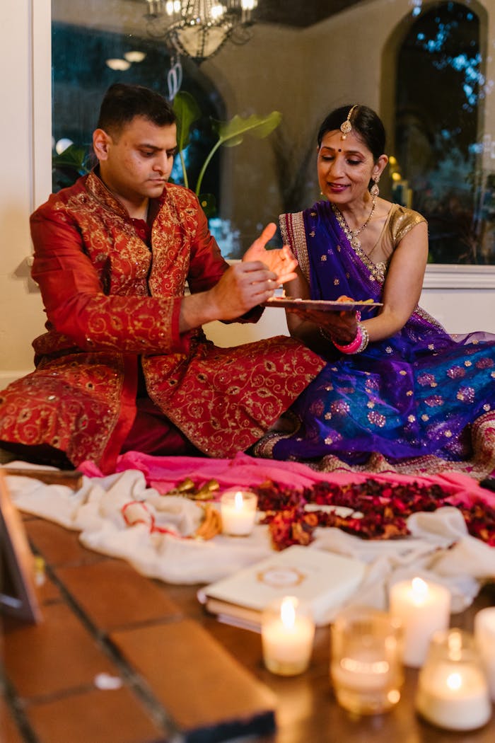 A couple in traditional clothing celebrating Diwali indoors by lighting candles.